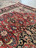 Antique Persian area rug flat lay showcasing a vibrant berry field framed by dark contrast floral borders.