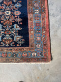 Corner view of antique Malayer rug displaying warm tones and botanical-inspired central column.