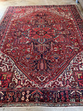 Hand knotted Persian Heriz rug. Antique geometric wool rug featuring stemmed flowers, serrated leaves, and a striking brick red field.