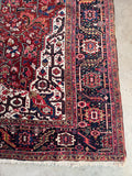 Corner view of heavy wool Persian Heriz rug with rich crimson, navy, coral, and camel tones.