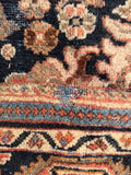 Antique wool Persian rug border detail showing faded floral patterns against deep charcoal blue.