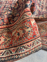 Antique Persian rug close-up showing blossoms and vines in ivory border.