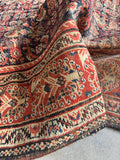 Antique Persian rug close-up showing blossoms and vines in ivory border.