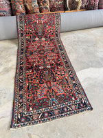 Narrow vintage Persian runner with peacock-like floral motifs and warm coral abrashed ground.