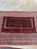 Hand-knotted Yomut tribal rug display with dark moody burgundy tones and traditional tribal geometric motifs.