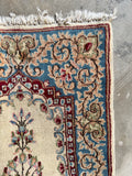 Corner view of small ivory and blue floral Persian rug with cranberry red flowers.
