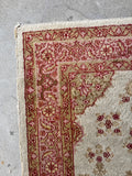 Corner view of small Turkish floor rug featuring a floral and geometric turtle border on a clean off-white ground.