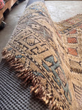 Hand knotted antique rug close-up view displaying worn wool pile and fringe edges.