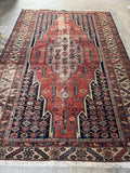 Distressed vintage Persian rug featuring aged rust, ivory, and deep navy vegetable dyes with a central medallion.