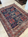 An antique square nomadic rug with geometric motifs, predominantly in blue and red, with a wool foundation.